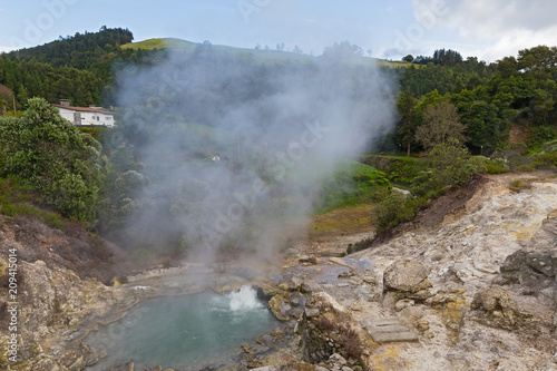 Hot spring surrounded by volcanic terrain and mountainous landscape in Furnas, Azores, Portugal. Summer landscape of Azorean village on a cloudy day.