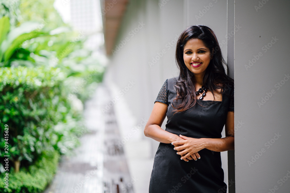 A successful Indian woman executive smiles and poses in a corridor for her  professional head shot