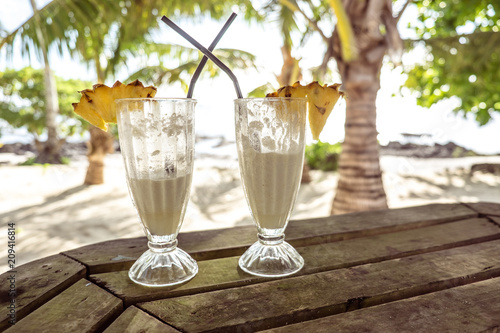 Half full glasses of tropical pina colada cocktail drink with pineapple garnish in glass with straws at exotic beach at Lefaga, Upolu Island, Samoa, South Pacific photo
