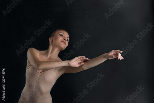 the beautiful ballerina in a beige suit from latex dances on a dark with light background in studio © rozaivn58