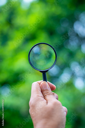 Hand holding magniflying glass see tree