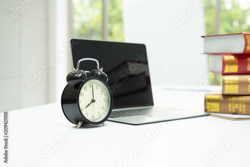 Clock, laptop and book are on the table in work area