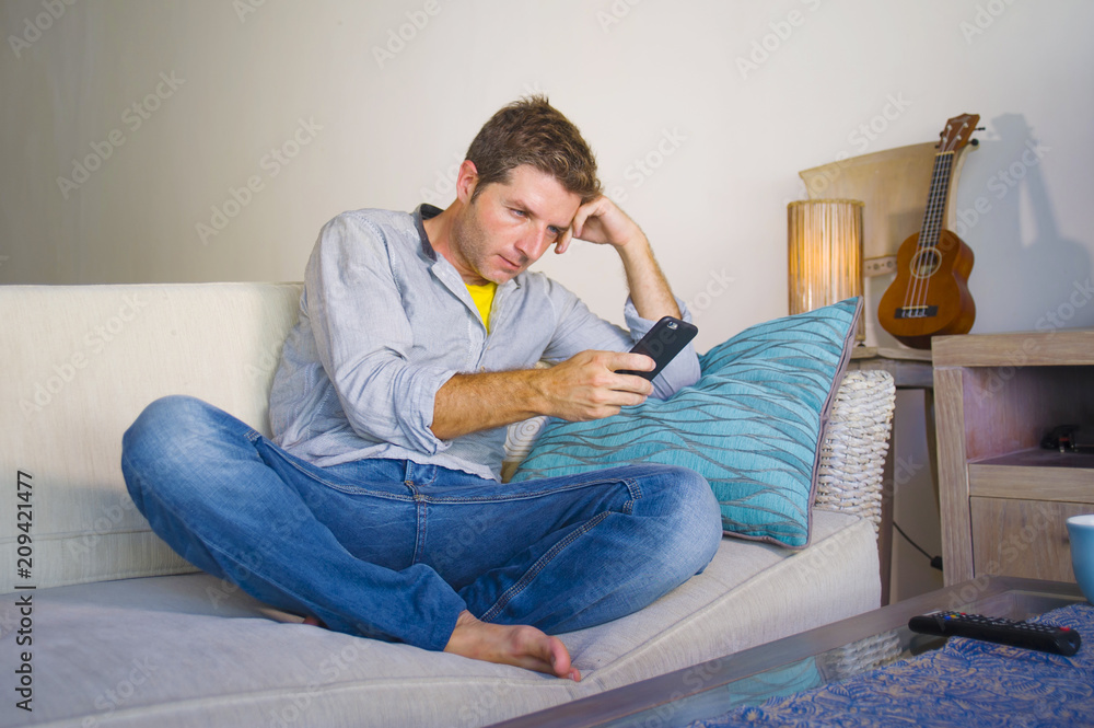 cool attractive and happy man sitting at living room sofa couch networking relaxed enjoying internet social media app using internet mobile phone