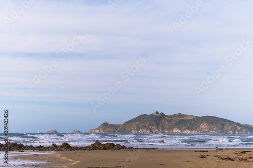 A scene of a beach on a cloudy day with mountain and road to the lighthouse  Nugget point  the Catlins  New Zealand