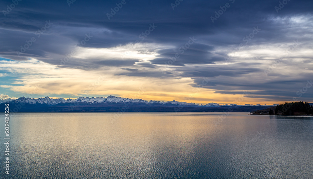 Calm lake scene at sunrise with snow capped mountains behind