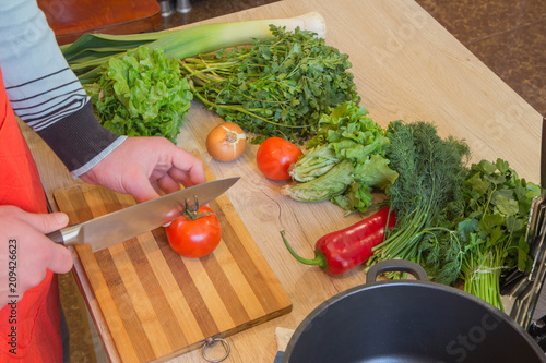 Man cooking healthy meal in the kitchen. Cooking healthy food at home. Male in kitchen preparing vegetables. Chef cuts the vegetables into a meal