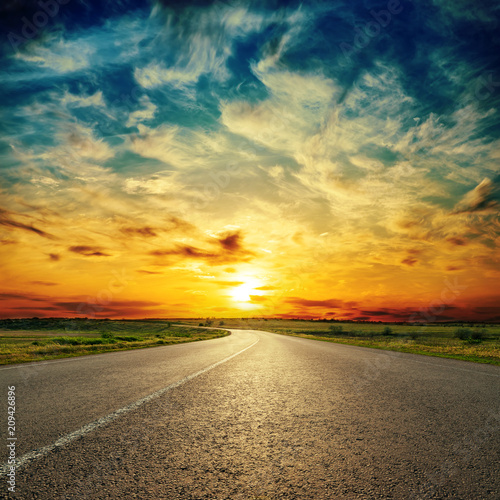 orange sunset in low dramatic clouds over asphalt road