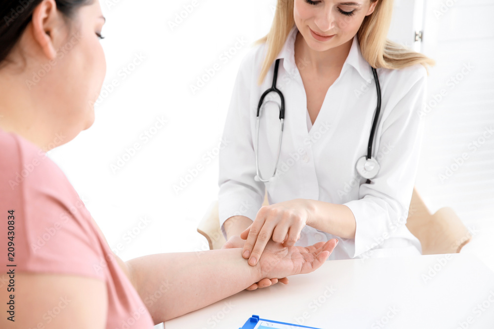 Female doctor taking pulse of overweight woman in clinic Female doctor taking pulse of overweight woman in clinic