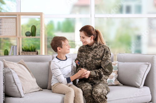 Woman in military uniform with her little son on sofa at home photo