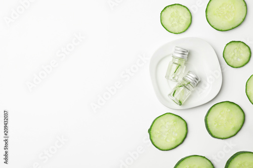 Flat lay composition with fresh cucumber skin care tonic and bottles on white background