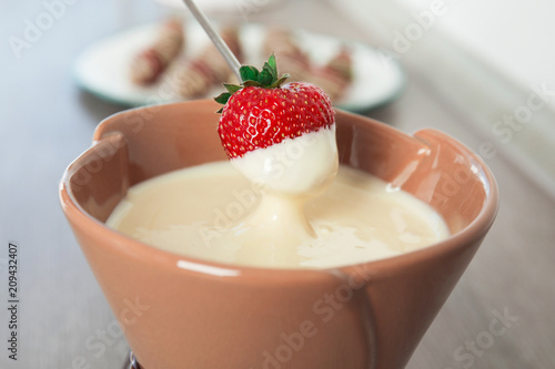 Fotografie Ripe strawberry dipping into white chocolate fondue, closeup
