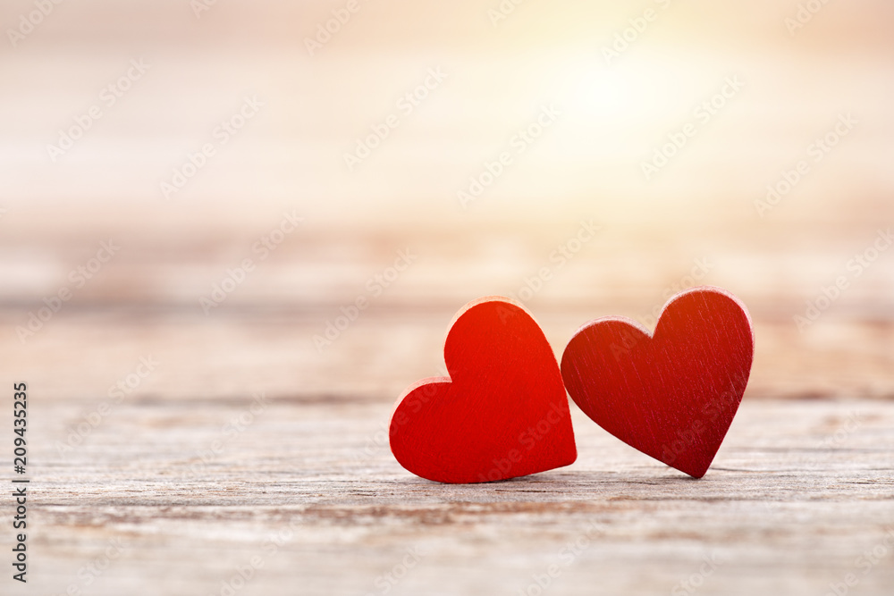 Fototapeta premium Two red hearts on wooden background in sunset