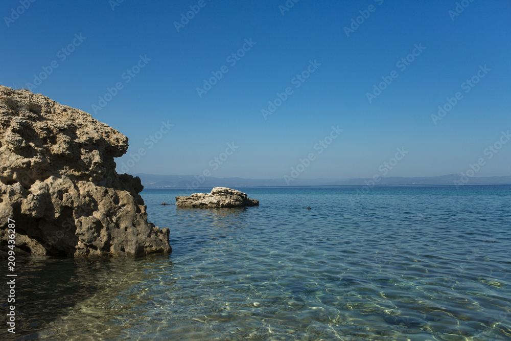 Stony shore on idyllic seascape. Rock in sea water on sunny blue sky. Wild nature, environment and ecology. Holiday destination and travelling. Summer vacation and wanderlust