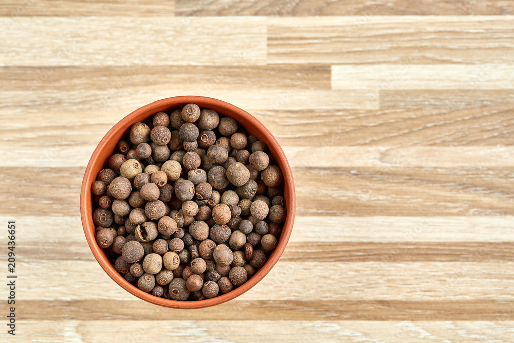 Clay bowl with dried allspice berries on textured wooden background, top view, close-up, macro, selective focus. Clay bowl with dried allspice berries on textured wooden background, top view, close-up, macro, selective focus.