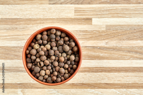 Clay bowl with dried allspice berries on textured wooden background  top view  close-up  macro  selective focus.