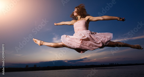 Fashion art portrait. Beautiful woman dancer in dress jump at sky background.