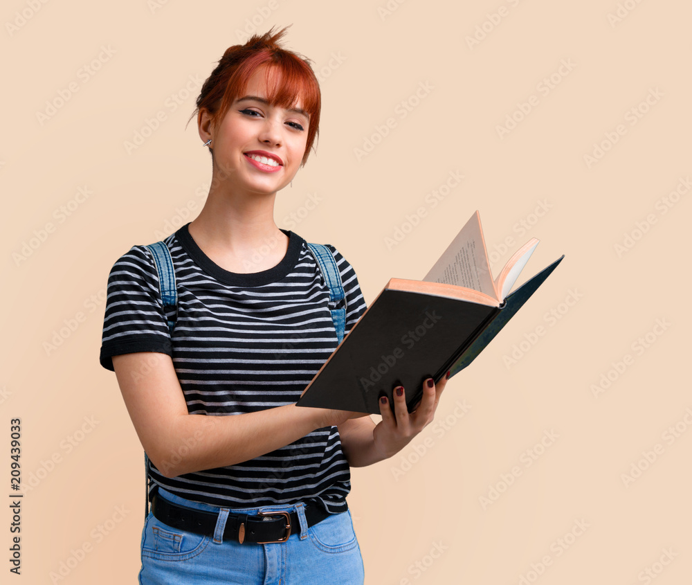 Young student redhead girl reading a book on ocher background Young student redhead girl reading a book on ocher background