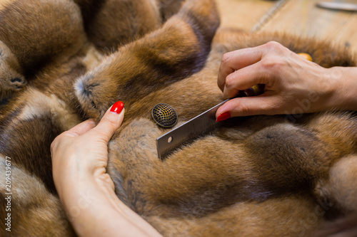 Professional tailor, designer combing fur coat at atelier, studio. Fashion and tailoring concept