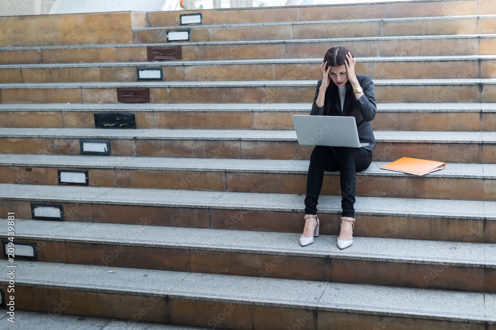 A businesswoman sit on the stairs and her hands clasped head,the feeling of stressed, sadness or displeasure caused by the non fulfillment of one's hopes or expectations. A businesswoman sit on the stairs and her hands clasped head,the feeling of stressed, sadness or displeasure caused by the non fulfillment of one's hopes or expectations.