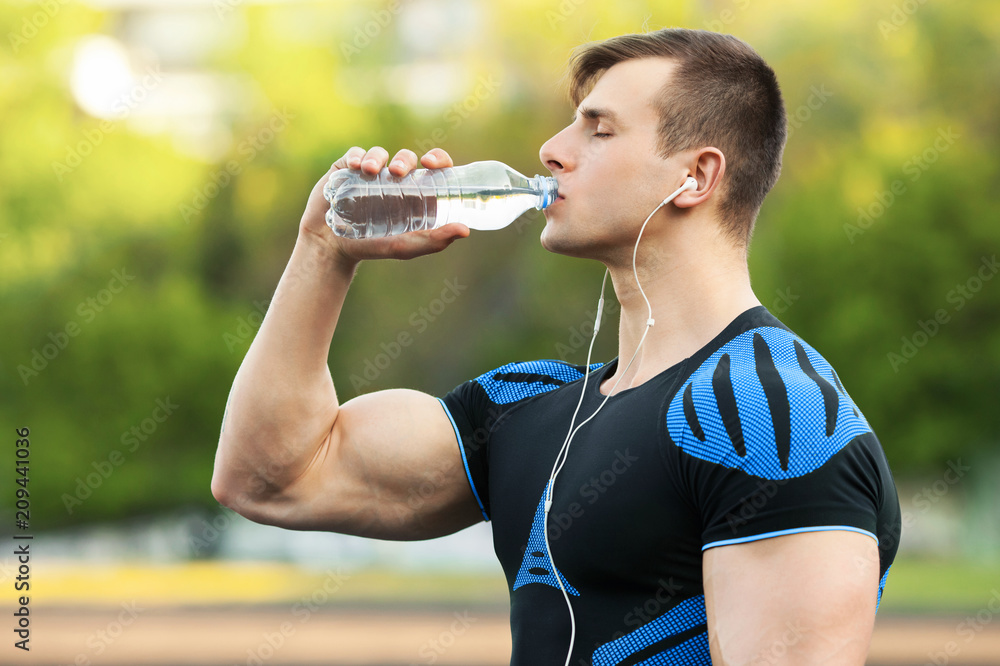 Active man drinking water from a bottle, outdoors. Young fit male quenches thirst Active man drinking water from a bottle, outdoors. Young fit male quenches thirst