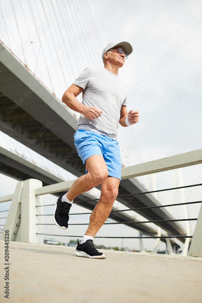 Obraz premium Aged man in sportswear running along bridge in urban environment on summer morning