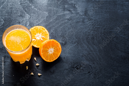 Orange juice in glass with raw oranges on black background. Copy space
