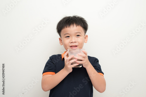 Young boy drinking chocolate milk isolated on white wall background.