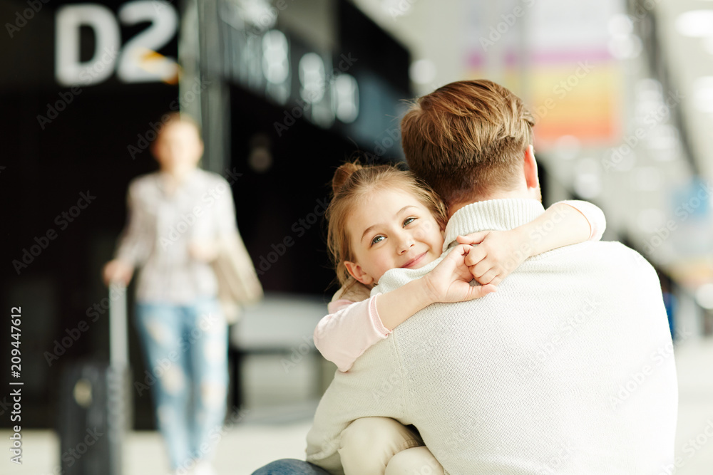 Naklejka premium Happy little girl embracing her dad in airport lounge after arrival with mother
