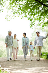 Happy family of five enjoying sunny day in park while taking walk and talking