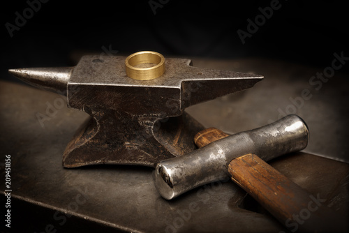 golden ring on an anvil and a goldsmith hammer in the jewelry workshop, still life with copy space in the dark background