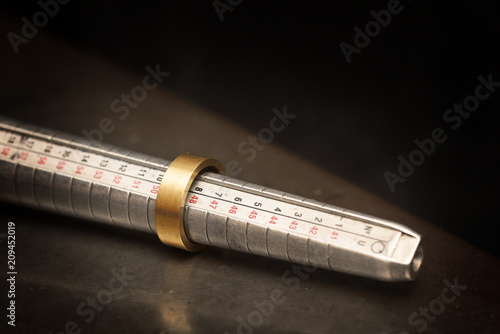 golden ring  on a ring sizer gauge, jeweler sizing tool from steel against a dark background with copy space photo