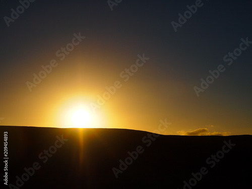 Shilloutte of a Mountain as the sun sets behind  with a clear sky