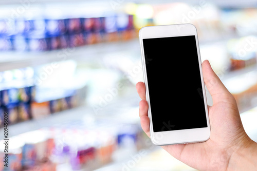 Hand using smart phone with blank screen over blur supermarket, store background, banner, business and technology, grocery online shopping, e-commerce template background
