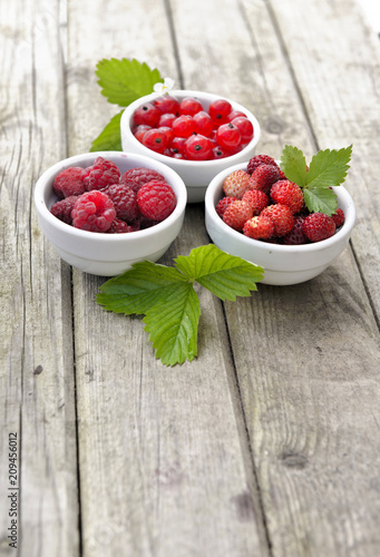 view on three little bowls on a wooden table full of red berries 