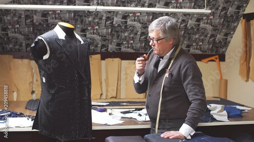 Professional mature tailor working on his new classical suit using tailor's dummy at his workshop looking at camera. photo