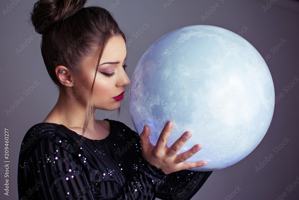 Naklejka premium Beautiful young elegant woman holding a moon sphere ornament. Retouched, studio lighting, dark colors and moody feel.