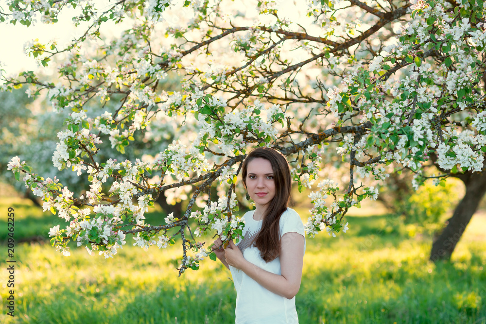 Portrait of young woman in spring garden. Beautiful girl and blooming apple tree on sunny day Portrait of young woman in spring garden. Beautiful girl and blooming apple tree on sunny day