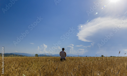 A young guy standing in the middle of a wheat field