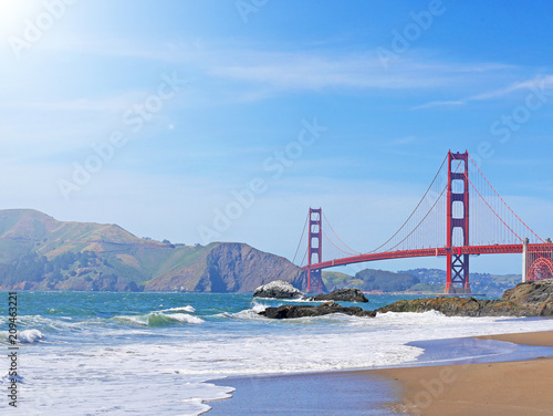 View of Baker beach in San Francisco seeing landmark red Golden Gate Bridge and Marin Headlands in the background on a sunny day with blue sky and sunlight rays
