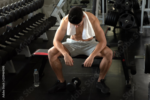 Portrait of sport young fitness man with white towel on his neck, relax after exercise at indoor sport gym, healthy sport concept.