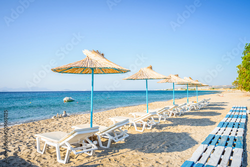 Fototapeta Naklejka Na Ścianę i Meble -  Beaches, Greece, Kos Island, Kardamena: beautiful holiday setting on a secluded beach with umbrellas on the Greek Aegean Sea with turquoise waters and a picturesque bay and islands in the background