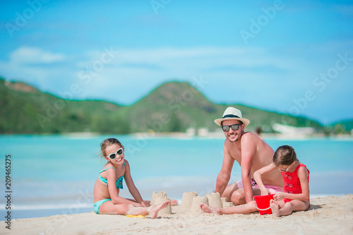 Family making sand castle at tropical white beach. Father and two girls playing with sand on tropical beach