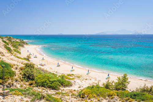 Fototapeta Naklejka Na Ścianę i Meble -  Beaches, Greece, Kos Island, Cap Helona: beautiful holiday setting on a secluded beach with umbrellas on the Greek Aegean Sea with turquoise waters and a picturesque bay and islands in the background