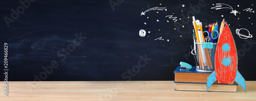 Back to school concept. rocket and pencils over open book in front of classroom blackboard.