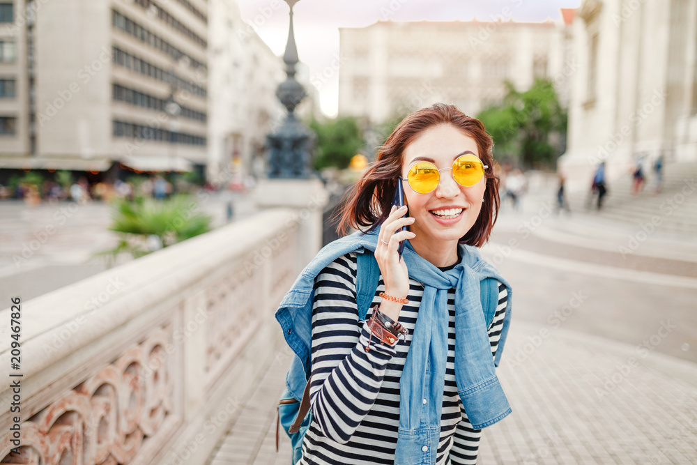Fototapeta premium Pretty young asian woman with backpack speaking on the phone outdoors in the city street