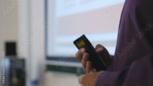 Close-up of hands men keep a clicker to show slides on a big screen in the audience