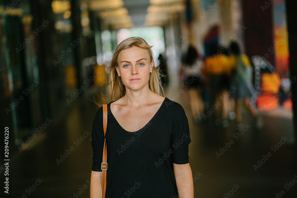 An attractive blonde woman looking fierce as she strikes a pose in front of the camera. She is wearing comfortable clothes and enjoys strolling inside her campus.