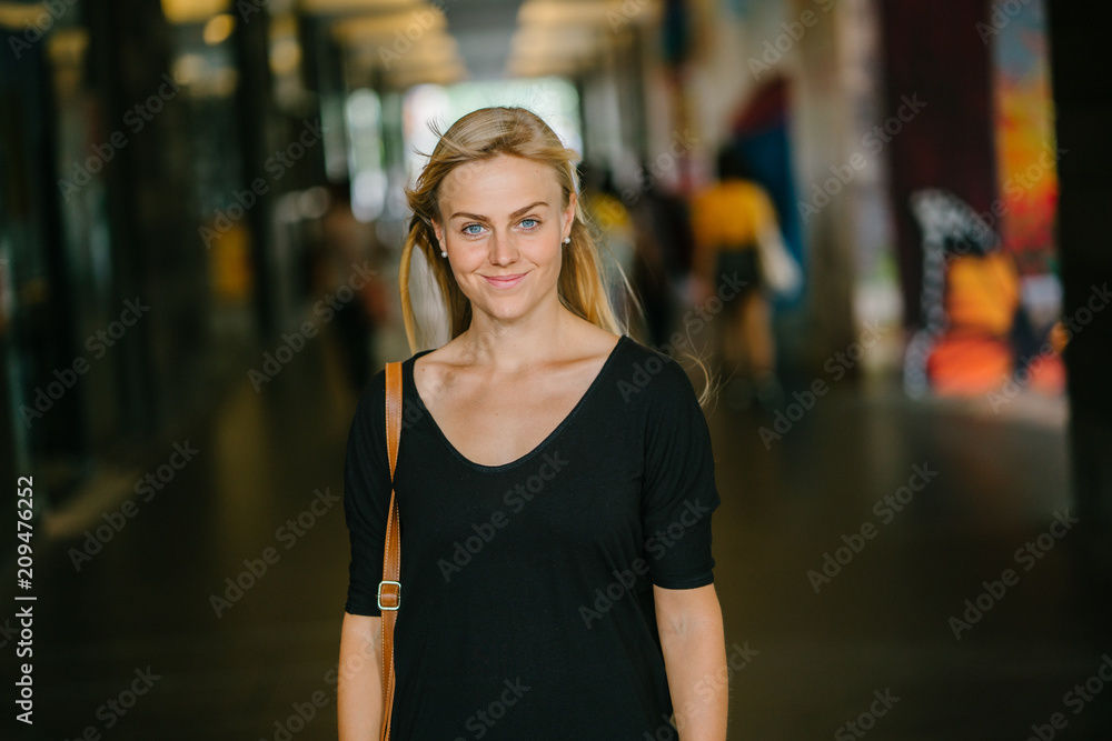 Portrait of a young, attractive, and photogenic blonde woman striking a fierce pose as she stands in the hallway of her campus. She is wearing casual and very comfortable clothes.