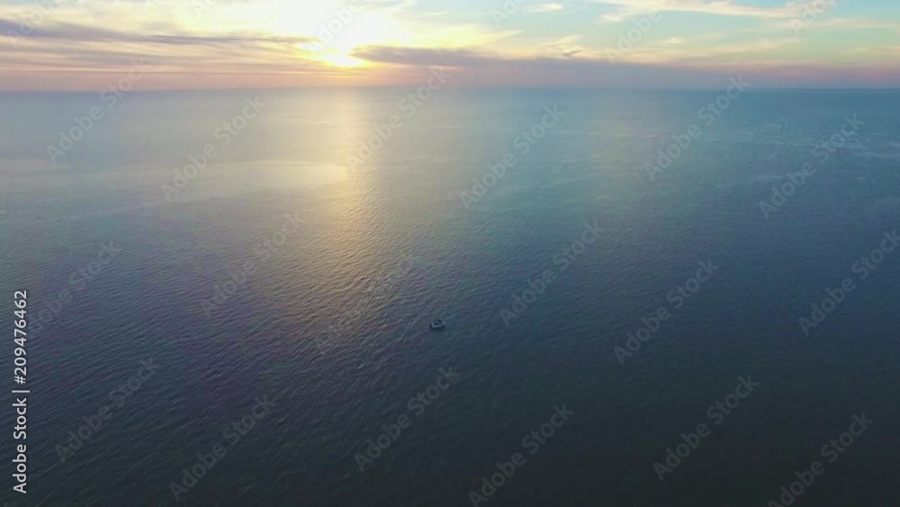 Descend over tranquil sea water surface and lonely fishing boat at sunset Descend over tranquil sea water surface and lonely fishing boat at sunset