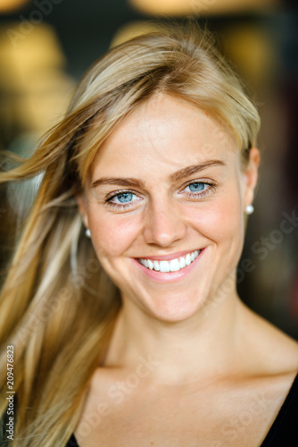 Portrait of a young and beautiful blonde woman with blue eyes standing and smiling in a corridor on a campus in Asia. She is casually dressed in light clothing.
